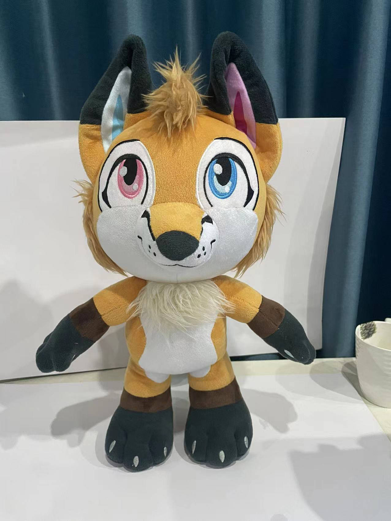 Front view of a plush fox with orange fur with accent colors patterned after the inclusive pride flag