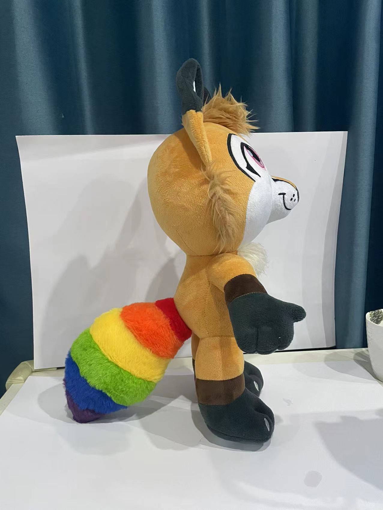 Side view of a plush fox with orange fur with accent colors patterned after the inclusive pride flag